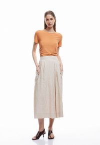 Orange kortærmet top parret med en flydende, kremfarvet, plisseret nederdel. Outfittet har lommer og brune hæl-sandaler.