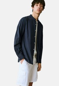 Námornícky košeľa s golierom a gombíkovým zapínaním, dlhé rukávy, v kombinácii s bielymi cargo šortkami s bočnými vreckami. Hladká textúra látky.