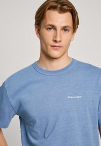 Plava pamučna majica s okruglim izrezom, kratkim rukavima i bijelim logotipom "Pepe Jeans" na prsima. Mekana tekstura i ležeran kroj.