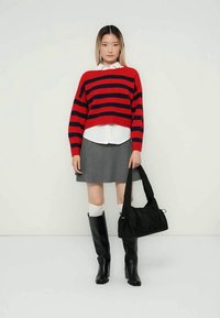 Rood- en marineblauw gestreepte cropped trui over een wit overhemd met kraag, gecombineerd met een grijze rok, kniehoge zwarte laarzen en een zwarte schoudertas.