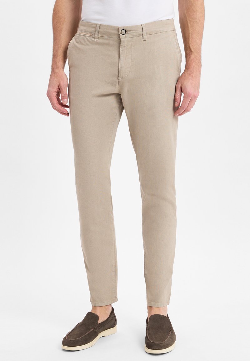 Beige chinos with a slim fit, cotton blend fabric, a single button closure, and front pockets. Paired with brown suede slip-on shoes.