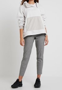 Světle šedý fleecový pulovr se zipovým límcem, s přední béžovou kapsou. Kombinován s elegantními šedými kalhotami a černými teniskami.