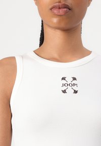Weißes, geripptes Tanktop mit einem zentralen, braun gestickten Logo "JOOP!" und floralem Akzent, rundem Halsausschnitt und ärmellosem Design.