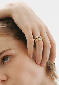Diseño de anillo de oro y plata con banda texturizada y acentos lisos, llevado en una mano que toca la cara, mostrando detalles y materiales.