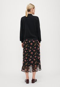 Black blouse with long sleeves, worn over a black floral-printed maxi skirt featuring a ruffled hem. Dark brown shoes complement the outfit.