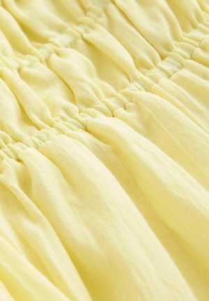 Lys gul stof med samlet tekstur, prydet med elastiske detaljer, der skaber et blødt, flydende udseende.