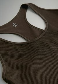 Camiseta sin mangas marrón con textura acanalada, cuello redondo y tirantes anchos. Cuenta con una etiqueta con el nombre de la marca. La tela parece elástica con una superficie texturizada.