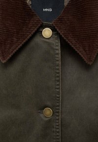 Veste vert foncé avec un col en velours côtelé marron, des boutons dorés et des coutures visibles le long de l'ouverture avant.
