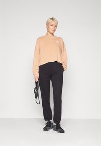 Top lungo in cotone oversize color pesca con logo, abbinato a pantaloni neri con vita elasticizzata e sneakers nere texturizzate.