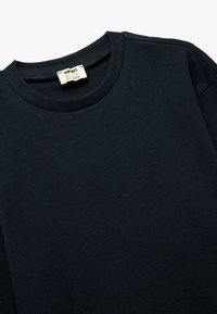 Camisa de manga larga de un azul marino oscuro con un patrón texturizado de punto waffle, que presenta un escote redondo y una etiqueta en el cuello.