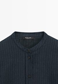 Camicia a righe verticali blu scuro con colletto rotondo e tre bottoni neri, con etichetta Massimo Dutti all'interno del collo.