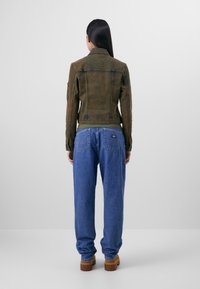 Pruun denim-jakk, millel on istuv disain, krae ja õmblused õlgadel, koos vabade siniste teksade ja pruunide jalatsitega.