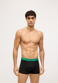 Bolsas de boxeo negras con una cinturilla verde que presenta el logo "TOMMY HILFIGER". Fabricadas en algodón con una textura suave y un diseño de tiro medio.