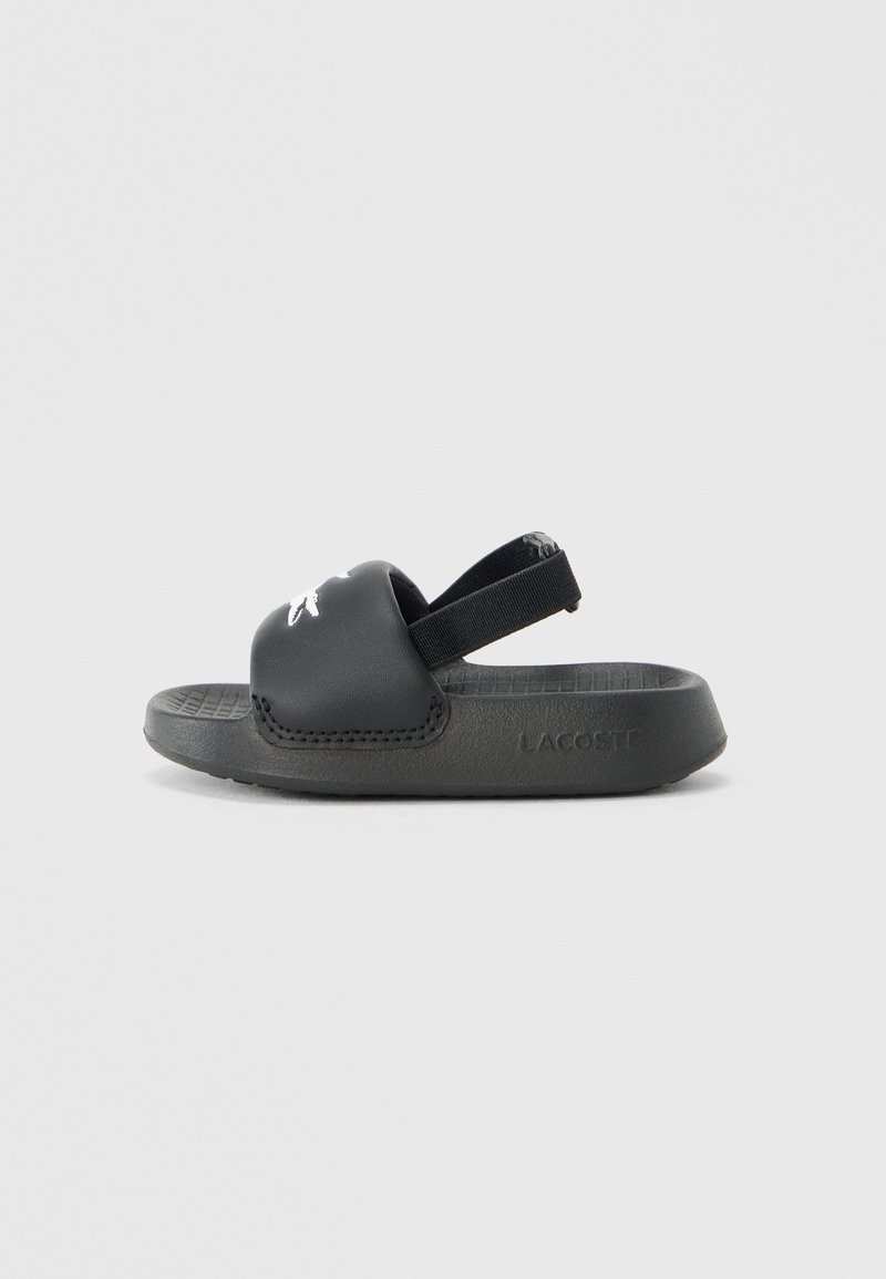 Μαύρο σανδάλι slides από καουτσούκ με ελαστικό λουράκι πίσω. Διαθέτει υφασμένο πέλμα και λευκό λογότυπο Lacoste στο πάνω μέρος.