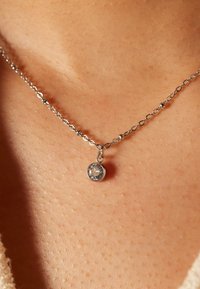Zilveren ketting met een ronde hanger waarin een heldere edelsteen omringd door een zilveren rand, rustend op de huid.