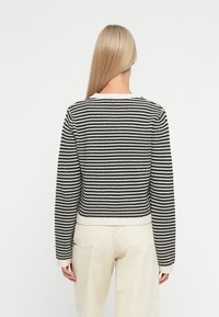 Maglione a zigzag bianco e nero con scollo a girocollo e polsini a coste, abbinato a pantaloni chiari. Vista posteriore mostrata.