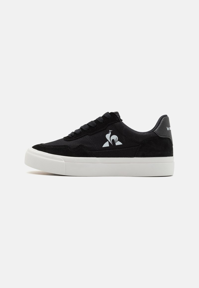 Baskets noires en combinaison de toile et de daim, avec une semelle en caoutchouc blanche et un logo sur le côté. Design à lacets.