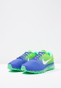 Baskets Nike Air Max en bleu et vert, avec une tige en mesh respirant, une semelle coussinée et des accents de logo blancs. Éléments de design texturés.