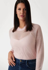 Lichtroze gebreide trui met lange mouwen en een sheer, geometrische halslijn, gecombineerd met donkerblauwe jeans met een sluiting aan de voorkant.