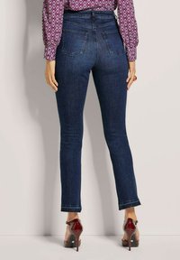 Hoge taille donkere blauwe jeans met een slim fit, voorzien van achterzakken en een rafelige zoom. Draagt met rode hoge hakken.