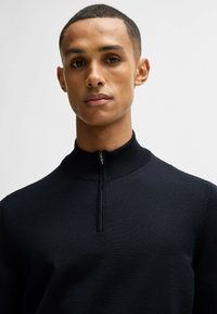 Maglione zip-up blu navy con collo alto, realizzato in tessuto a maglia testurizzato, con zip di lunghezza quadrante e dettagli a coste.