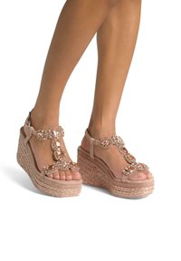 Sandali wedge beige con suola in juta intrecciata, impreziositi da grandi pietre preziose rosa e un delicato design a T-strap. Parte superiore in tessuto texturizzato.