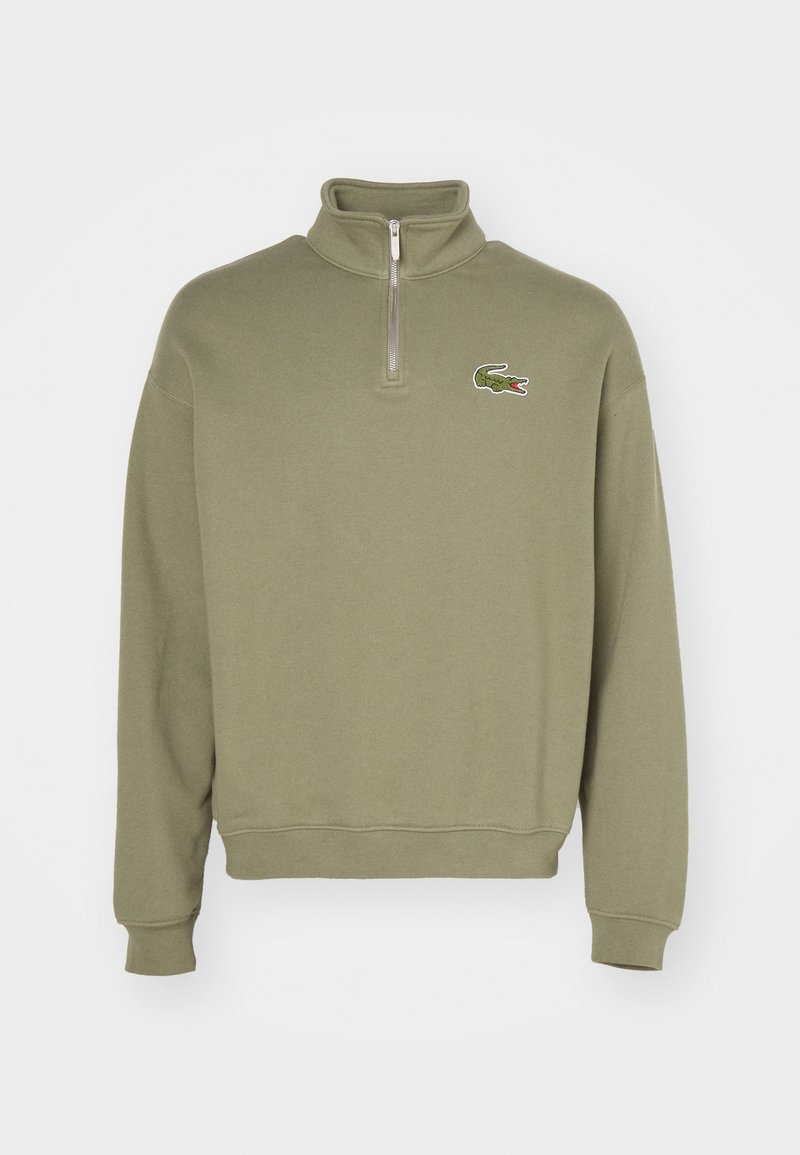 Sweat-shirt vert olive avec fermeture éclair quart de zip, poignets et ourlet côtelés, avec un petit logo crocodile brodé sur la poitrine gauche.