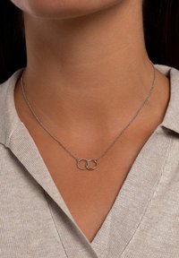 Silverhalsband med två sammanlänkade ringar; en är slät, den andra har en texturerad yta. Kedjan är delikat och verkar fin.