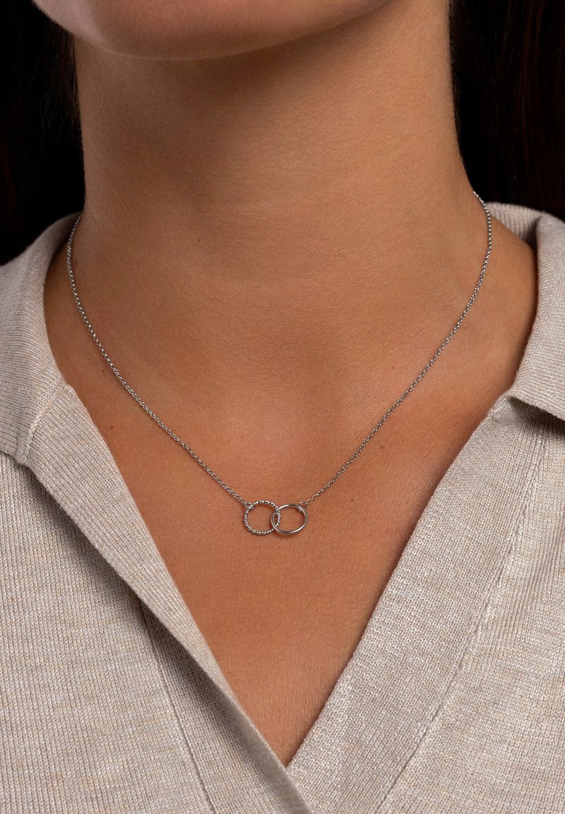 Silverhalsband med två sammanlänkade ringar; en är slät, den andra har en texturerad yta. Kedjan är delikat och verkar fin.