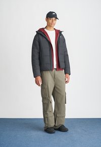 Mustat puffatakit, joiden päällä marjapunainen huppari, valkoinen t-paita, oliivinvihreät cargo-housut taskuilla ja mustat kengät. Yksinkertainen, rento muotoilu.