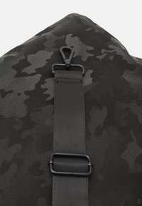 Czarny plecak w kamuflażu z teksturowaną powierzchnią, regulowanym paskiem oraz metalowym zapięciem. Trwała i praktyczna konstrukcja.