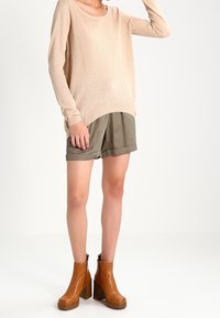 Beige stickad tröja, lös passform, rundad halsringning; olivgröna uppvikta shorts; bruna plattformsankelstövlar med hög klack.