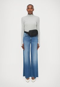 Borsa a cintura nera trapuntata indossata sopra un top a maniche lunghe grigio chiaro, abbinata a jeans blu a vita alta svasati e scarpe bianche con punta a forbice.