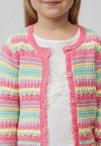 Mehrfarbige Strickjacke mit gewellten Kanten, die rosa, blau, gelb und lila Streifen aufweist. Vorn sichtbare Knöpfe und Spitzenverzierungen.