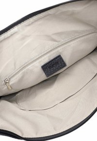 Interiér béžové látkové tašky s malou kapsou na zip a černou koženou štítkem s raženým nápisem "RUE 09."