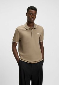 Beige polo skjorta med en mjuk textur, två knappar i placket och kontrasterande vit krage. Har "HUGO"-logotypen i vitt på bröstet.