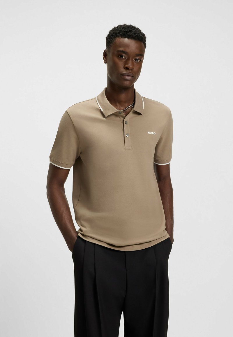 Beige polo skjorta med en mjuk textur, två knappar i placket och kontrasterande vit krage. Har "HUGO"-logotypen i vitt på bröstet.