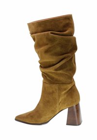 Botín marrón de ante hasta la rodilla con diseño holgado, punta afilada y un tacón grueso de color madera. Textura suave y acabado blando.