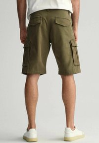 Pantaloni cargo verde oliva con più tasche, in materiale cotone, design fino al ginocchio e passanti per cintura, abbinati a sneaker bianche.