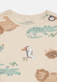 Camicetta corta beige chiaro con colletto rotondo che presenta illustrazioni colorate di animali tra cui un tucano, un leone e una tartaruga.