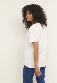 T-shirt bianca in cotone con una vestibilità comoda, maniche corte e scollo rotondo, abbinata a jeans in denim blu. Design semplice e minimale.