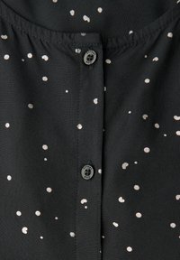 Tessuto nero con motivo a pois argentati, dotato di chiusura con bottone. Texture liscia con una leggera lucentezza, arricciato all'altezza del collo.