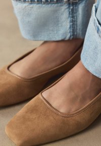 Brune ruskindssko med firkantet tå og et udskåret design på overdelen. Skoen har en glat overflade og minimal syning.