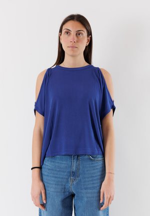 Top blu royal a maniche corte con design a spalla scoperta, in tessuto morbido, vestibilità ampia e scollatura rotonda. Abbinato a jeans di jeans rilassati.
