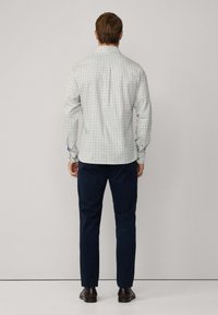 Geruite shirt in lichte tinten met blauwe en groene accenten, gecombineerd met marineblauwe broek. De stof lijkt zacht met een gladde textuur, lange mouwen geknoopt.