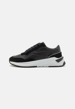 Sneaker sportivo nero con materiali misti: pelle liscia, accenti in camoscio e una suola in gomma bianca. Presenta una linguetta imbottita e lacci.