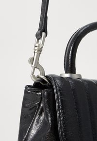 Sac à main en cuir noir avec une finition texturée, doté d'une poignée robuste et d'un fermoir en métal argenté pour attacher une sangle.
