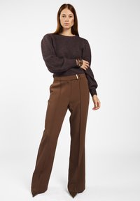 Bruine wijde broek met een soepele textuur en verticale plooien, gecombineerd met een donkerpaarse gebreide trui met pofmouwen.