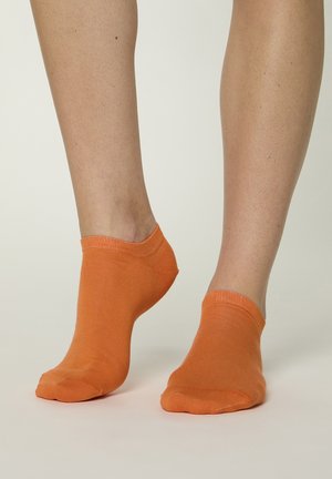 Füße mit niedrig geschnittenen orangenen Socken auf einer hellen Oberfläche, zeigen Beinhaare und natürlichen Hautton.
