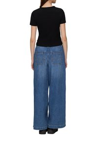 Schwarzes, kurzärmeliges Oberteil kombiniert mit weiten blauen Jeans; die Jeans verfügen über zwei Gesäßtaschen mit gewölbtem Nähedetail und einem lockeren Schnitt.